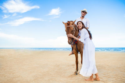 Couple with horse on shore at beach against sky