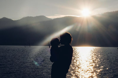 Mother and child kissing by lake on sunny day