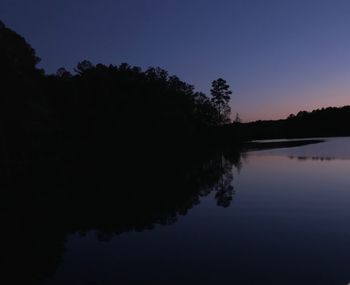 Silhouette trees by lake against sky during sunset