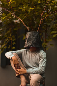 Midsection of man holding hat while standing against trees