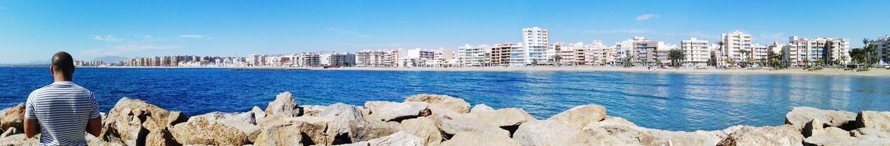 Panoramic view of sea and cityscape against blue sky