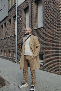 Full length of man holding smart phone standing against wall