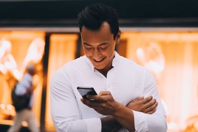 Young man using smart phone while standing in illuminated city