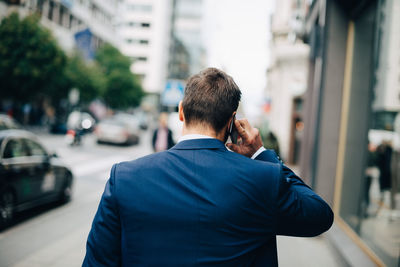 Rear view of mature businessman talking on mobile phone while walking on sidewalk in city
