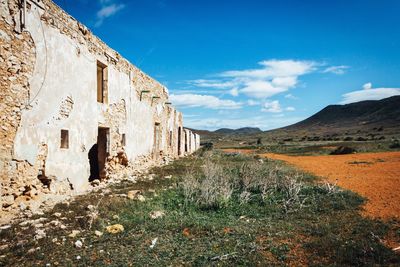 Abandoned building by field against sky in desert