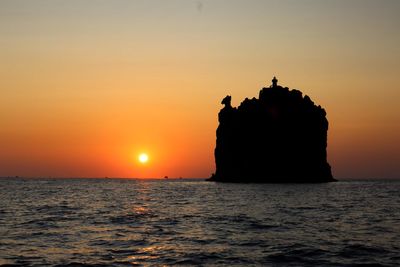 Silhouette rock in sea against sky during sunset