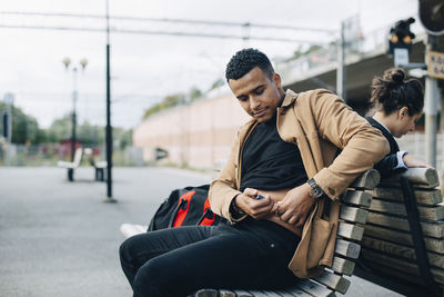 Man injecting insulin in abdomen while sitting on bench at railroad station platform