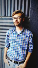 Portrait of man wearing eyeglasses standing against wall