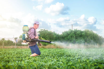Male farmer with a mist sprayer processes potato bushes with chemicals. protection of cultivated 