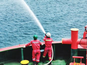 Rear view of firefighters spraying water while standing in nautical vessel