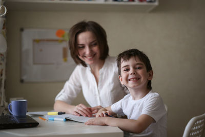 Beautiful woman tutor is engaged with a child boy at home at a table, real interior