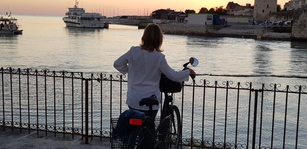 Rear view of woman on railing by river against sky