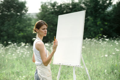 Young woman smiling while standing on field against trees