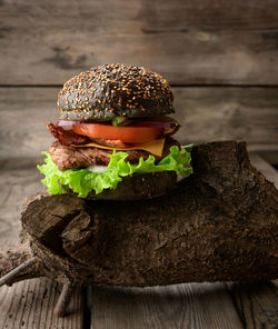 Cheeseburger with black bun, meat and vegetables on a wooden background, fast food