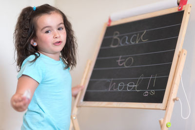 Portrait of smiling girl rubbing text from blackboard in classroom