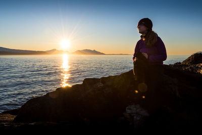 Woman standing on rock by sea against clear sky during sunset