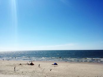 People on beach against clear blue sky