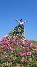 Low angle view of woman standing by flowers against clear sky