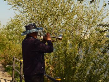 Man playing trumpet against trees