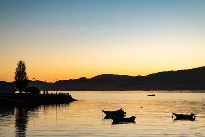 Silhouette boats in lake against clear sky during sunset