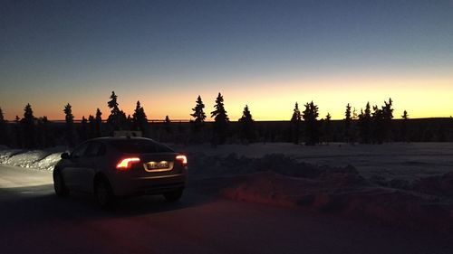 Cars on snow covered land against sky during sunset