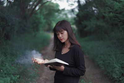 Portrait of woman holding sparklers in book while standing in forest