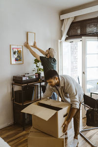 Man mounting frame on wall with boyfriend stacking cardboard boxes at home