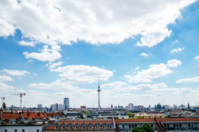 Fernsehturm amidst buildings in city against cloudy sky