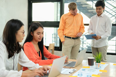 Women using laptops on desk while male colleagues discussing in office