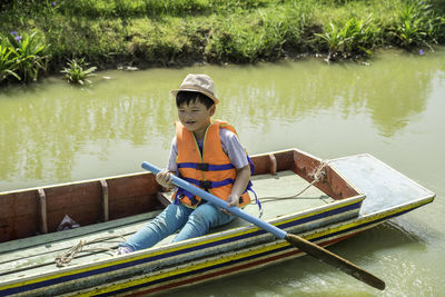 Full length of boy sitting on boat in lake