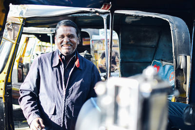 Portrait of smiling man standing against rickshaw