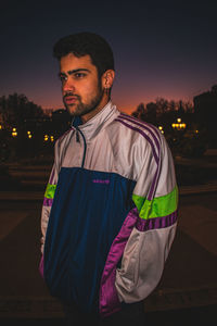 Young man looking away while standing against sky at night