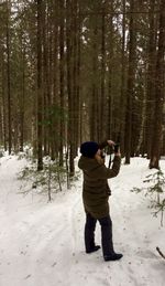 Woman photographing through camera at forest during winter