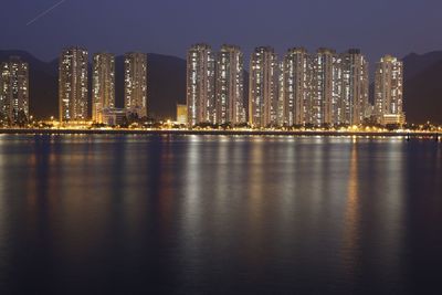 Illuminated city by sea against sky at night