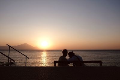 People sitting by sea against sky during sunset