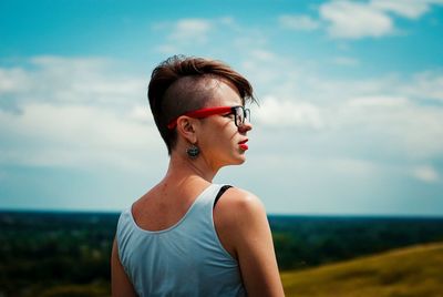 Rear view of thoughtful young woman looking away while standing against blue sky