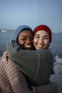 Happy young women embracing each other while standing against sky