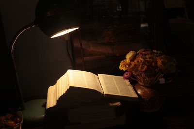 High angle view of illuminated lamp by open book on table