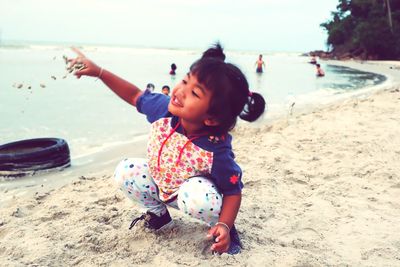 Cute girl crouching while playing with sand at beach