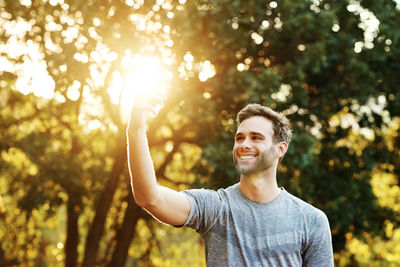 Portrait of young man standing against trees during sunset