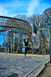 Full length of man jumping against trees in city