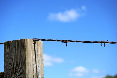 Barbed wire fence on wooden post against sky