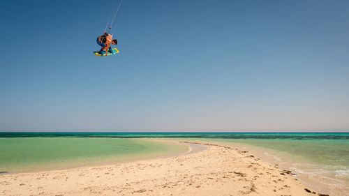 Full length of man kiteboarding in mid-air against clear sky