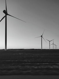 Silhouette wind turbines on field against sky