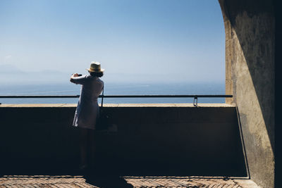 Full length rear view of woman photographing sea from observation point against clear sky