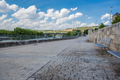 Footpath by street in city against sky