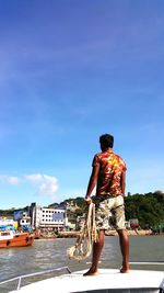 Rear view of man standing on yacht against sky