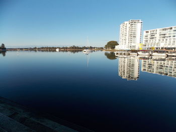 Reflection of buildings in lake against blue sky