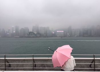Rear view of person with pink umbrella by river in city during monsoon