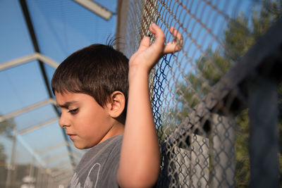 Side view of boy standing by chainlink fence